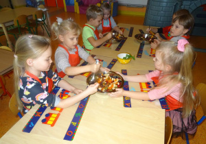 Grupa dzieci miesza łyżkami owoce w misce.